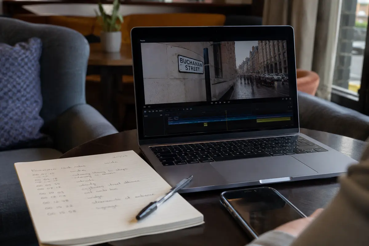 A laptop, editing timeline and handwritten timecodes sit in a Glasgow lounge after access is restored.
