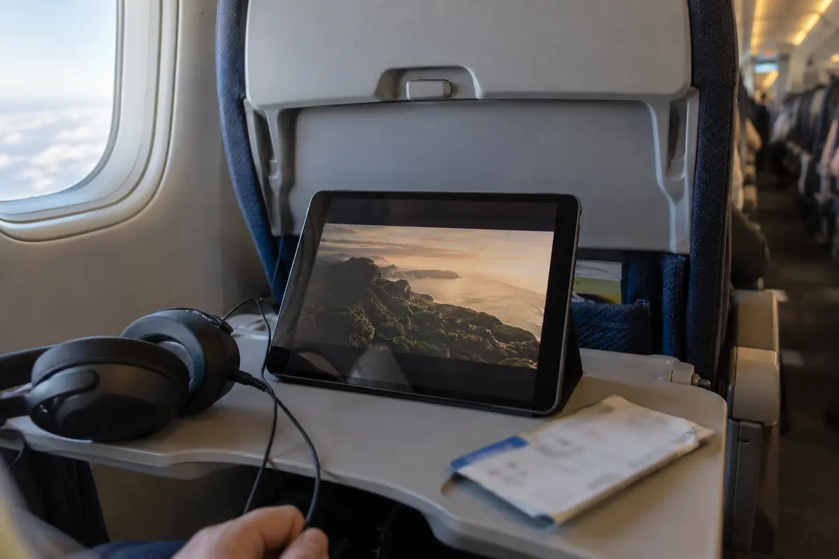 A downloaded film playing on a tablet at an airplane seat with headphones ready