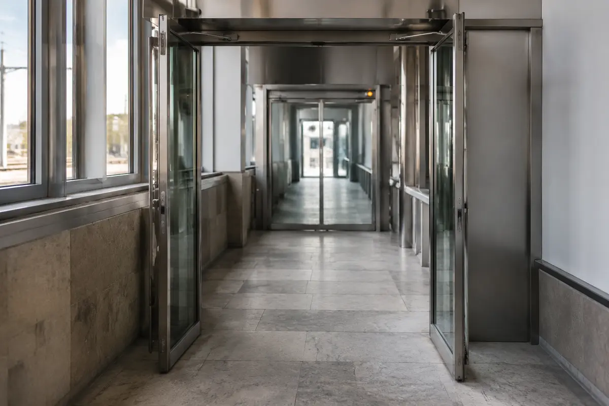 An open doorway leads to another closed checkpoint farther down a station corridor